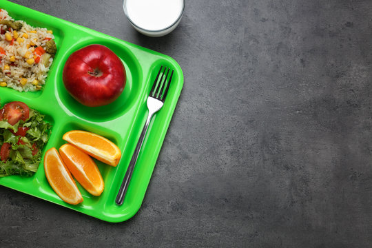 A green tray holds a balanced meal: rice, salad, apple, oranges, and milk.