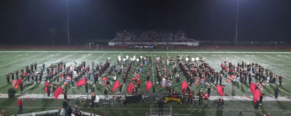 A marching band performs on a football field under the stadium lights.