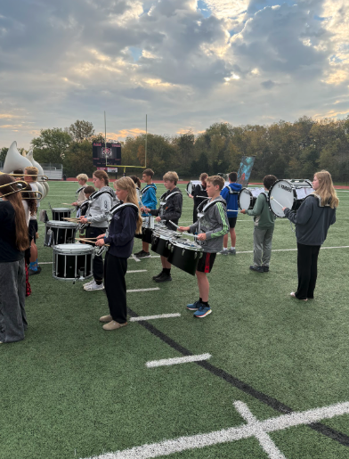 A marching band practices on a green football field under a cloudy sky.