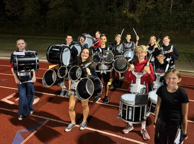 A group of young people pose with their marching band drums on a track.