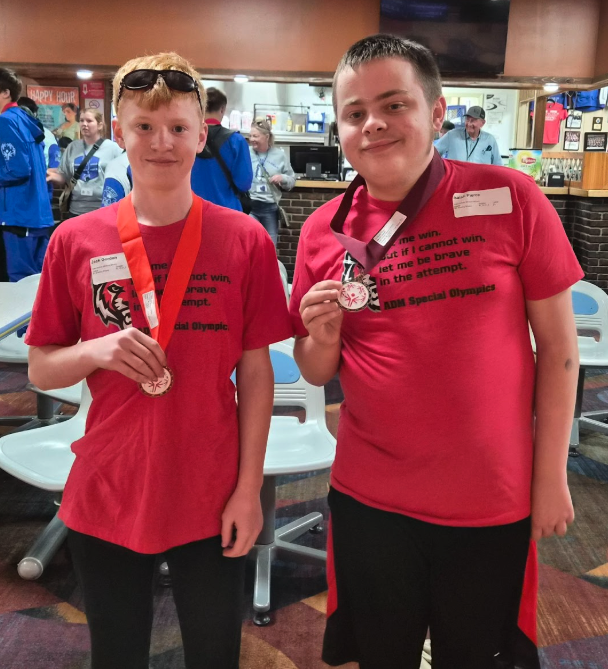 Two young men proudly display medals, smiling for the camera.