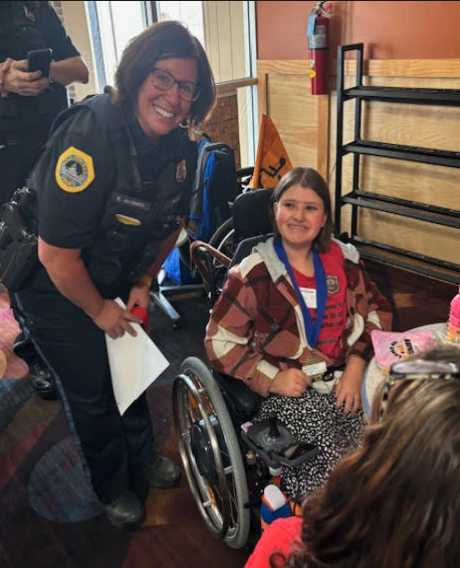 A police officer smiles and poses with a young girl in a wheelchair.