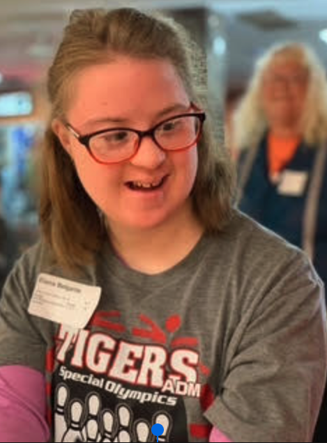 A young woman with glasses smiles, wearing a Special Olympics shirt.