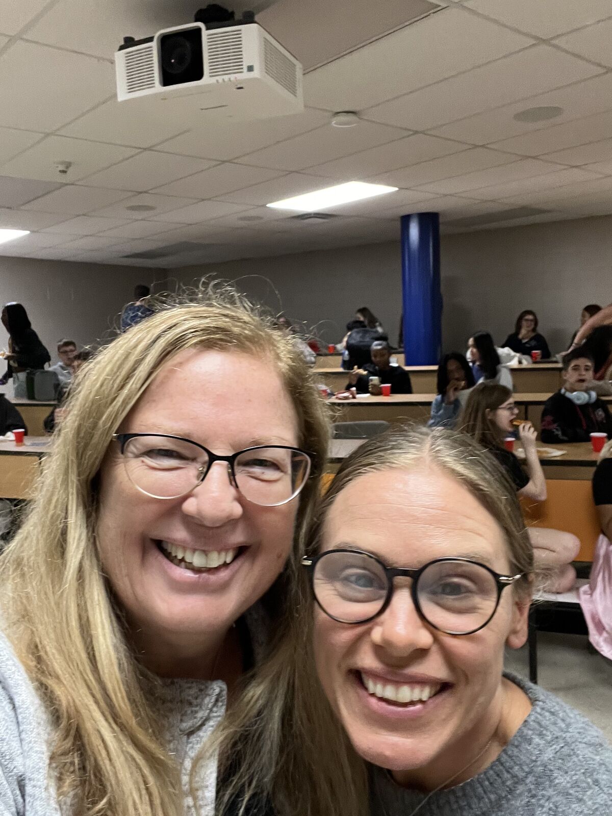 Two women smile at the camera, with other people in the background.