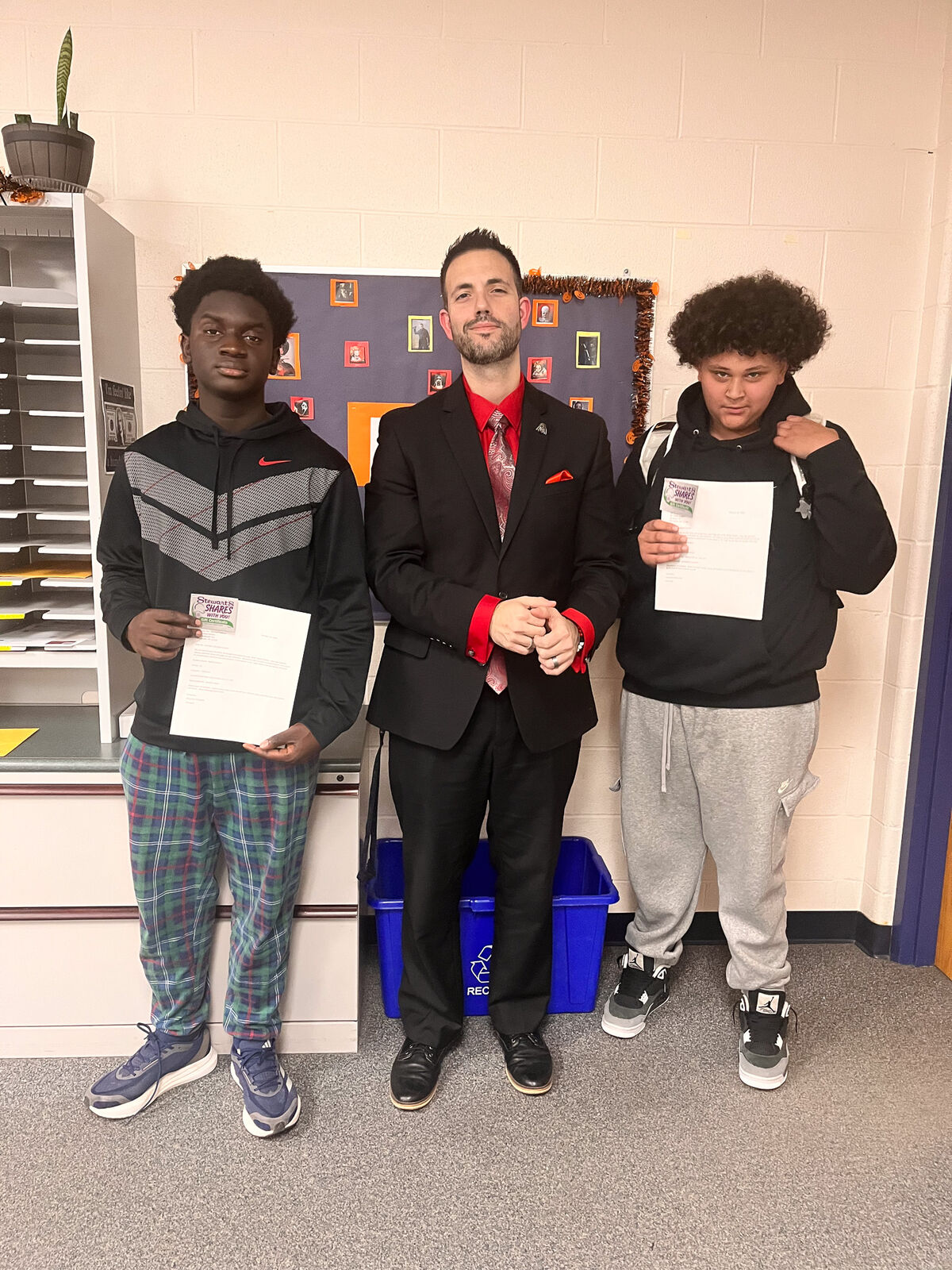 Three people stand together, holding papers, in a school setting.