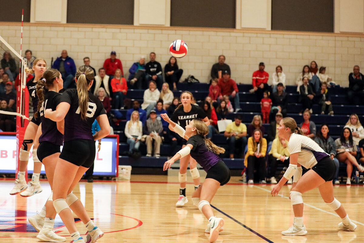 A volleyball game is in progress, with players in action on a wooden court.