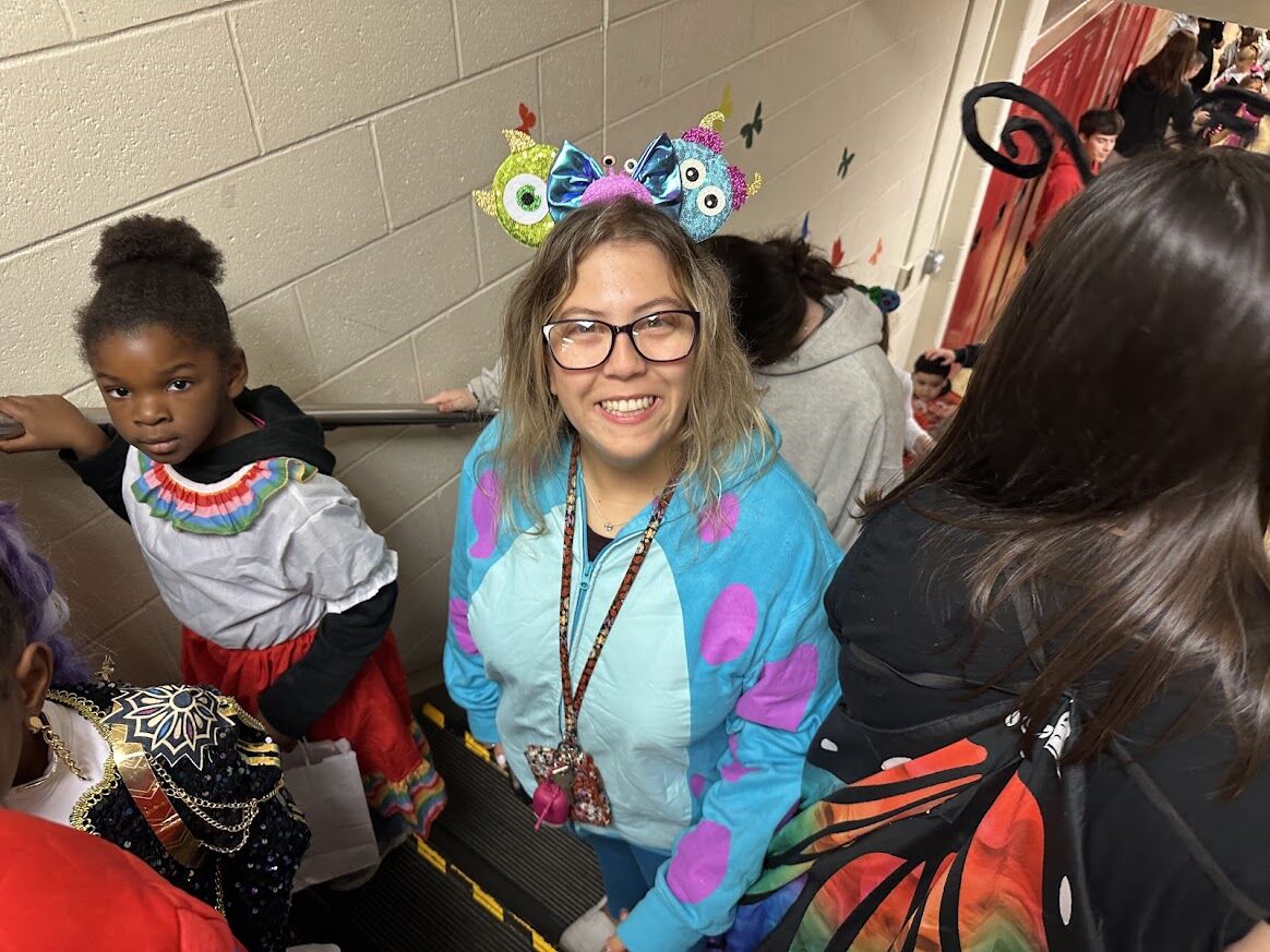 A woman in a blue monster costume smiles, wearing a headband with eyes.