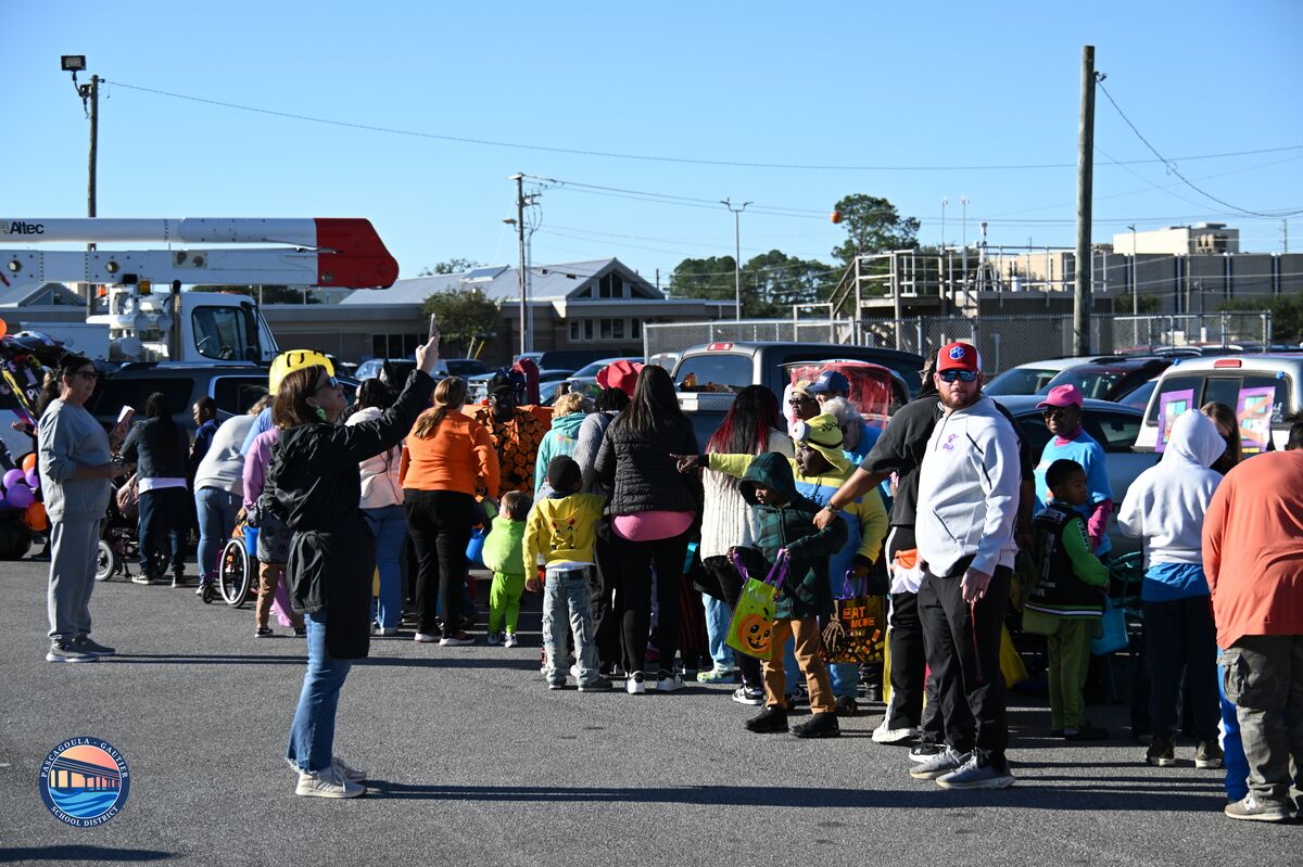 A crowd of people, including children in costumes, gather outdoors on a sunny day.