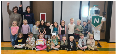 A group of children and adults pose with a mascot, celebrating a milestone.