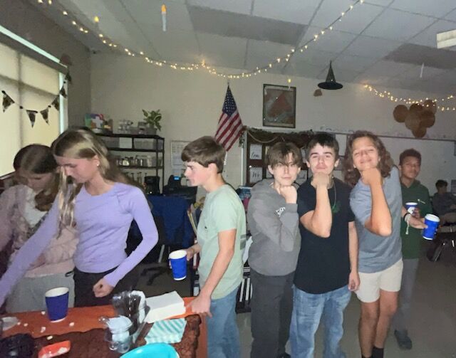 A group of students gather in a classroom, some holding cups.