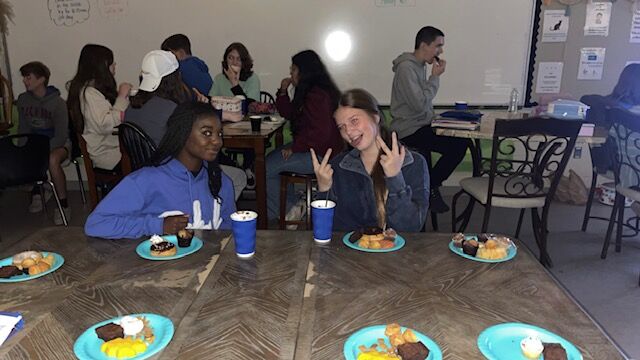 A group of students enjoy treats and drinks at a table in a classroom.