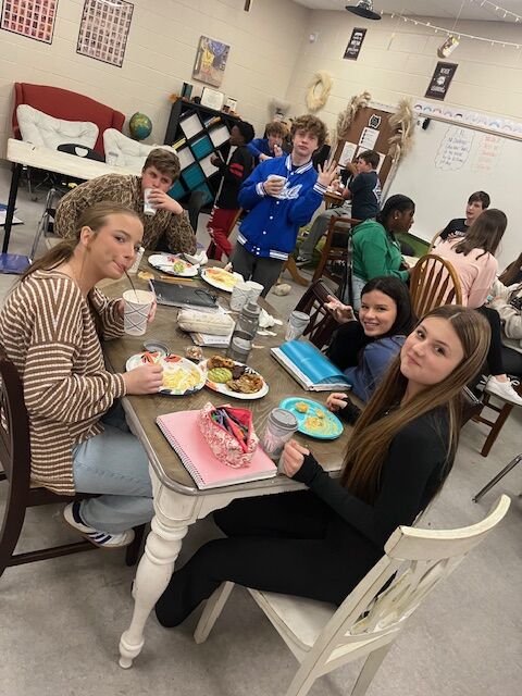 A group of students gather around a table, smiling and looking at the camera.