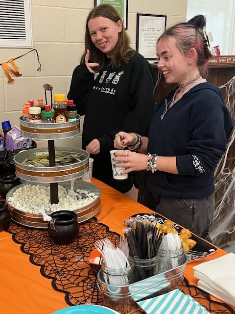 Two young people smile near a Halloween-themed snack table.