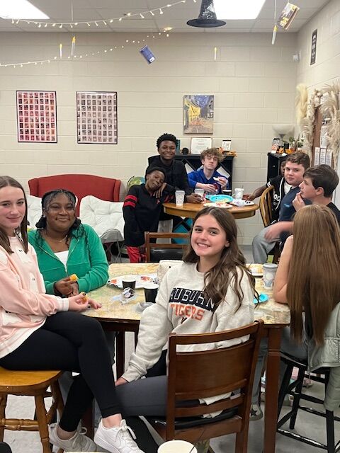 A group of students sit at tables, smiling and looking at the camera.