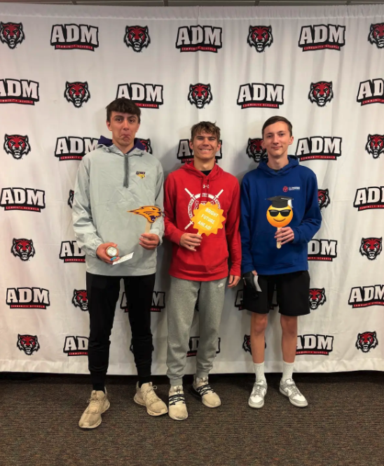 Three young men pose in front of a banner with school logos.
