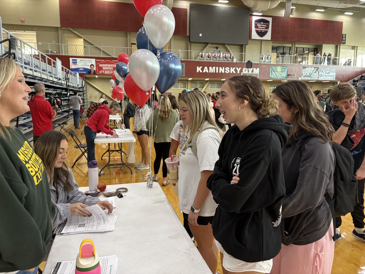 High school students gather around a table while counselors distribute scholarship information.