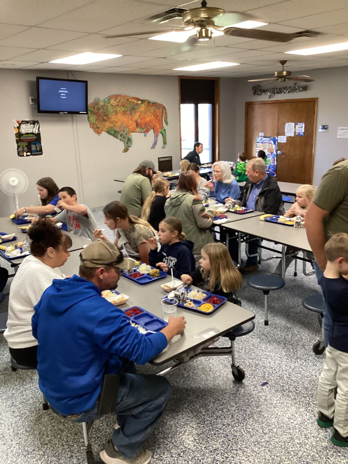 People eat lunch at tables in a cafeteria setting.