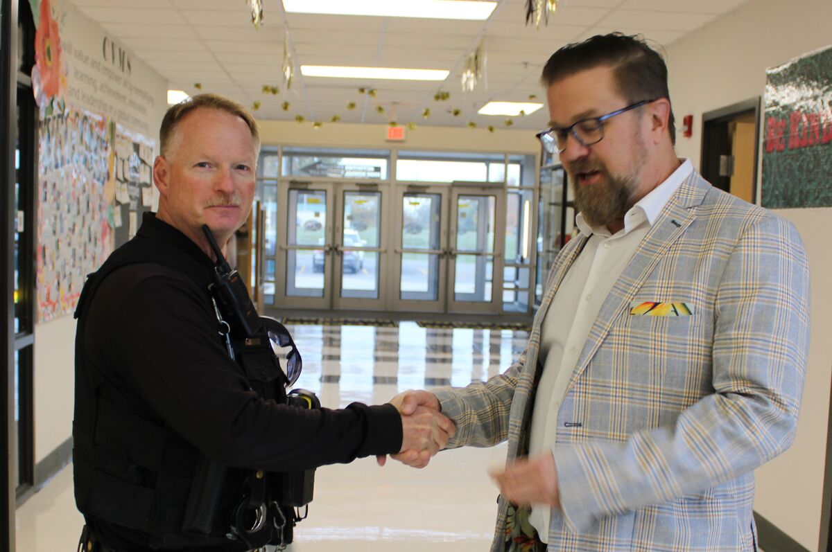 Dr. Robinson shakes hand with Officer Palmer as he is recognized for his military service - in the hallway of a school