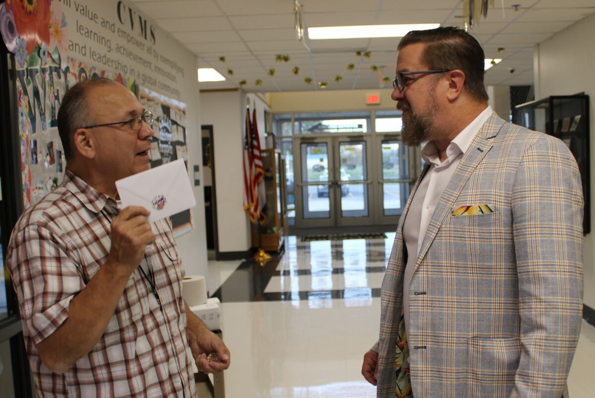 Staff member Mr. Bell talks with Dr. Robinson while holding a card in his hand, standing in the hallway of a school
