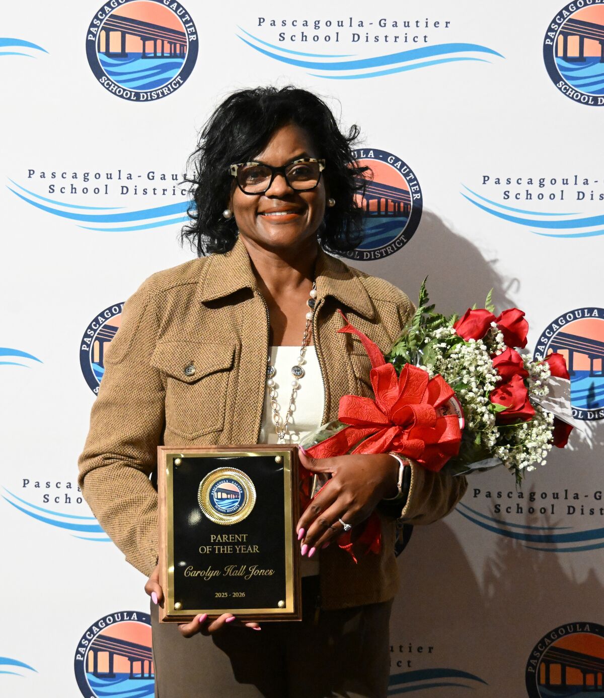 A woman smiles, holding a plaque and flowers, celebrating an award.