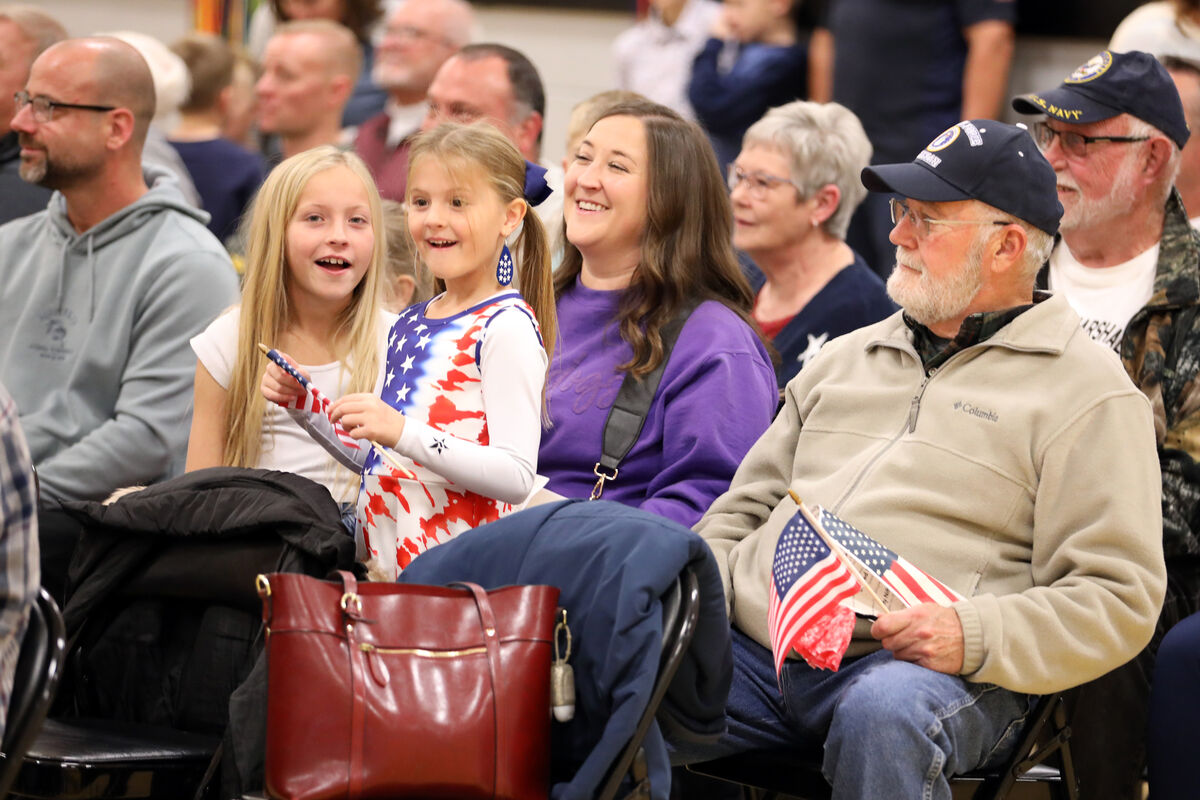 A crowd gathers, with people of all ages smiling and holding small American flags.