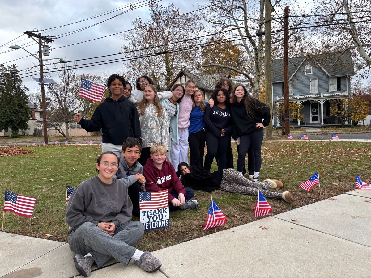 A group of diverse students pose with American flags, honoring veterans.