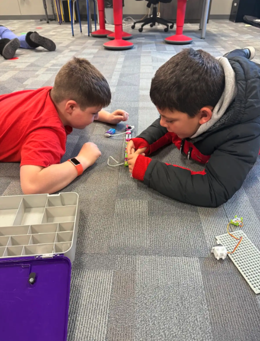 Two boys work together on a small building project on the floor.