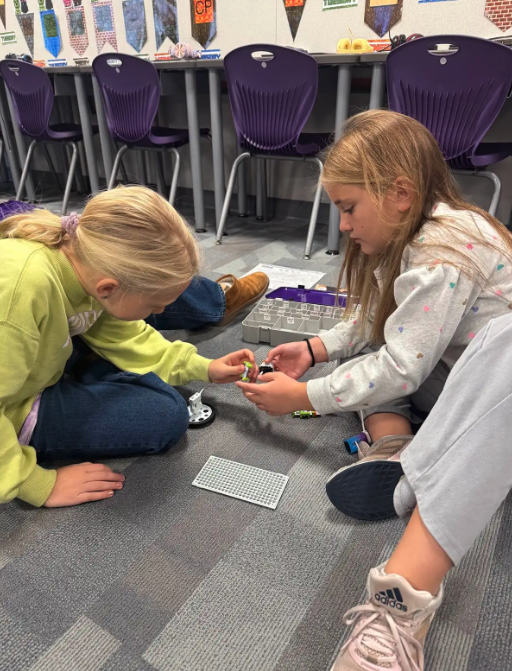Two young girls work together on a building project on the floor.
