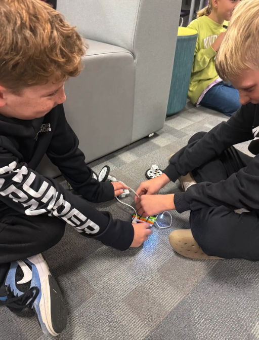 Two students work together on a small electronic project on the floor.