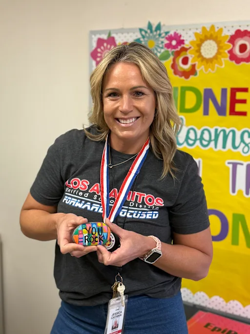 A smiling woman holds a painted rock that says 'You Rock'.