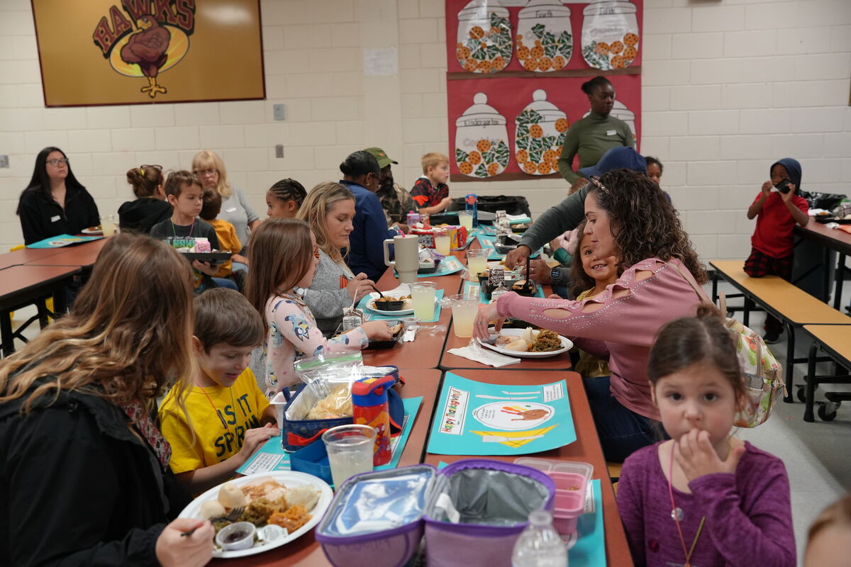Children and adults gather at tables in a school cafeteria.