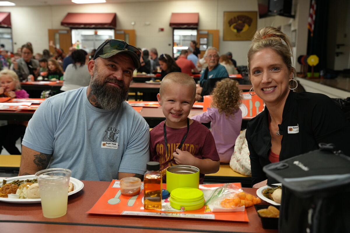 A family smiles at the camera while seated at a table in a cafeteria.