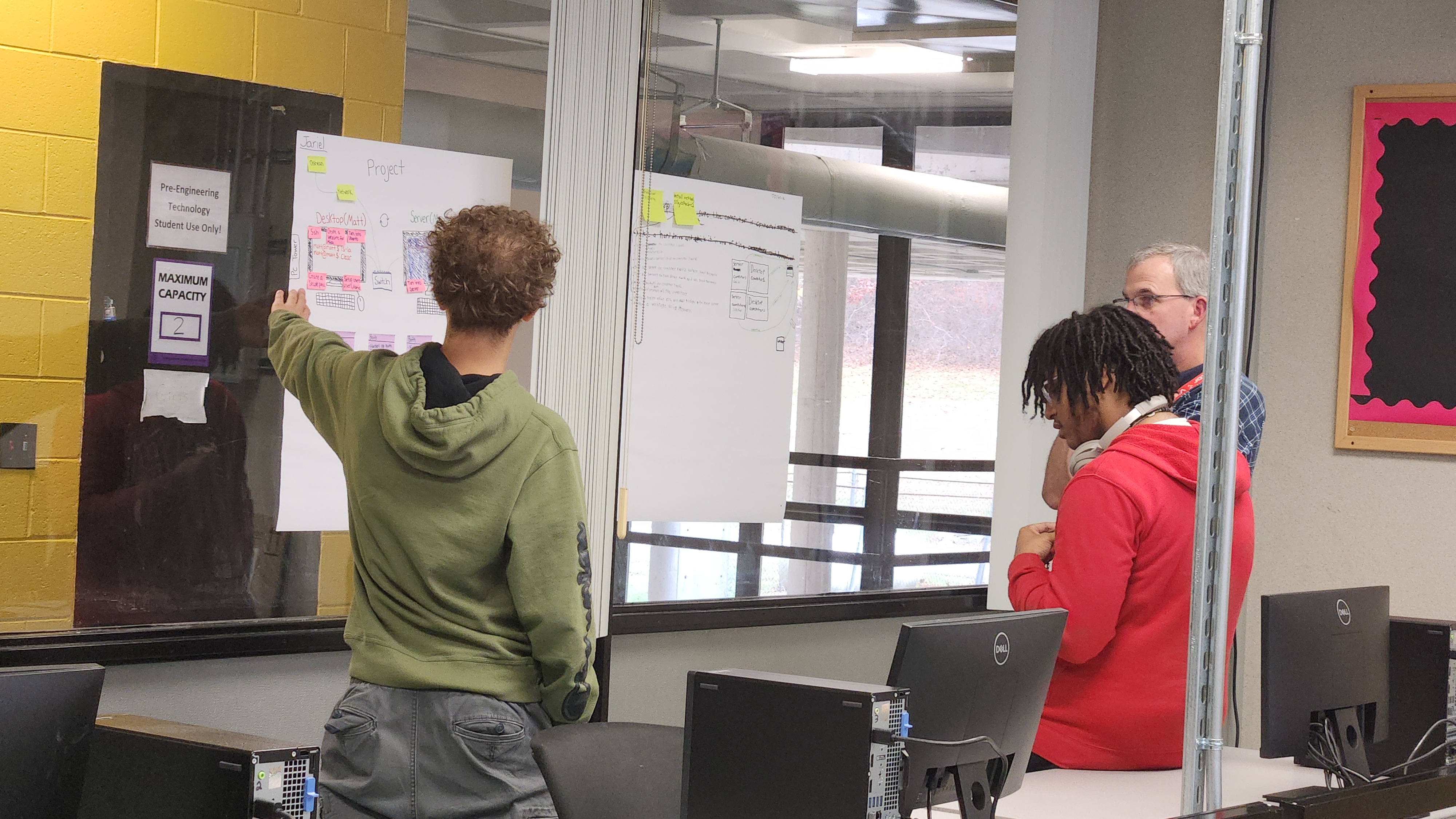 Jariel Mendez and Joshua Aracena with Patrick Laverty collaborate, reviewing a project diagram on flip chart paper..