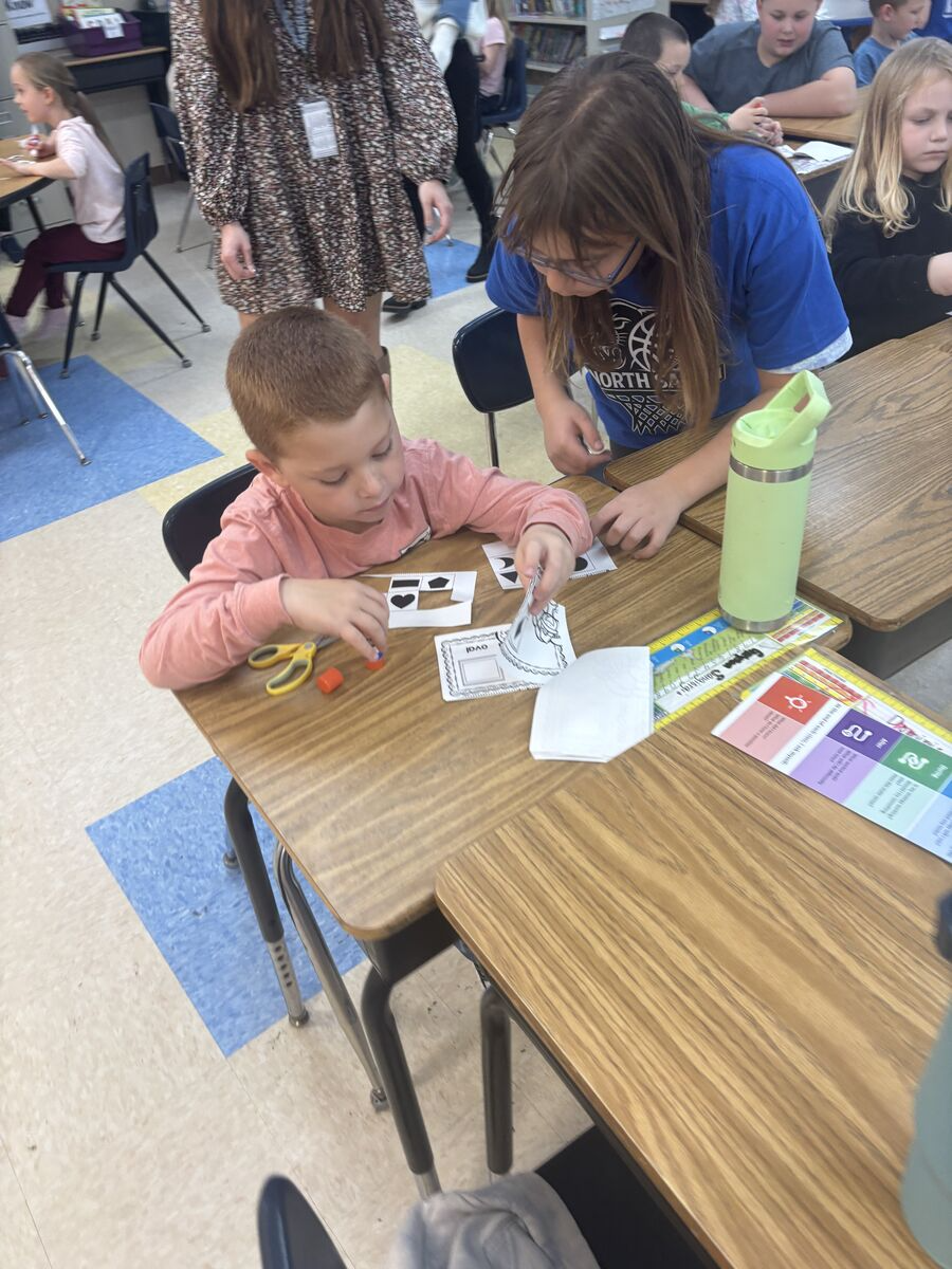 Two students work together at a desk, assembling a craft project.