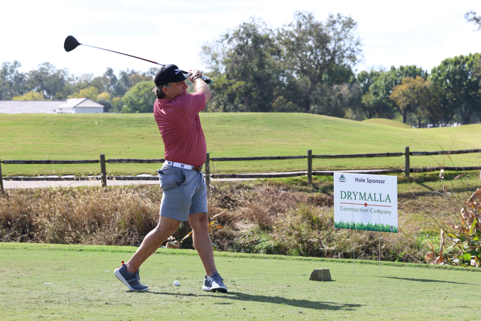 A golfer swings a club on a sunny golf course, preparing to hit the ball.