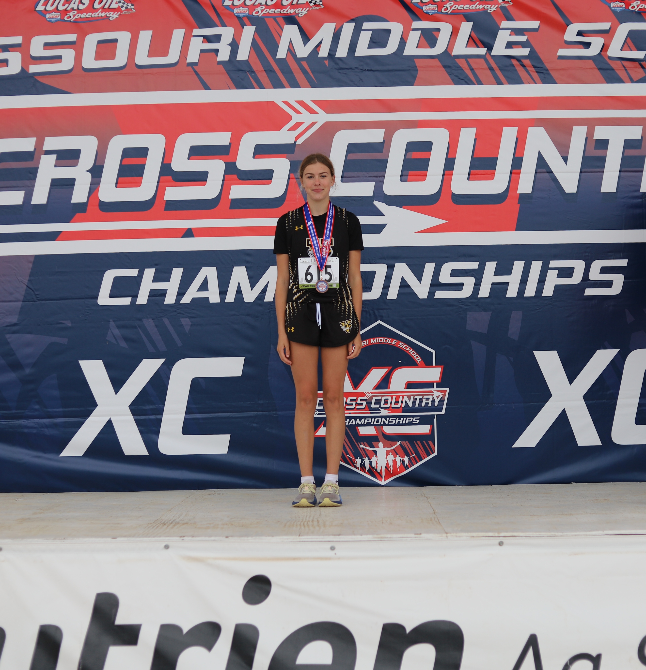 A young woman stands on a podium, wearing a medal and athletic attire.