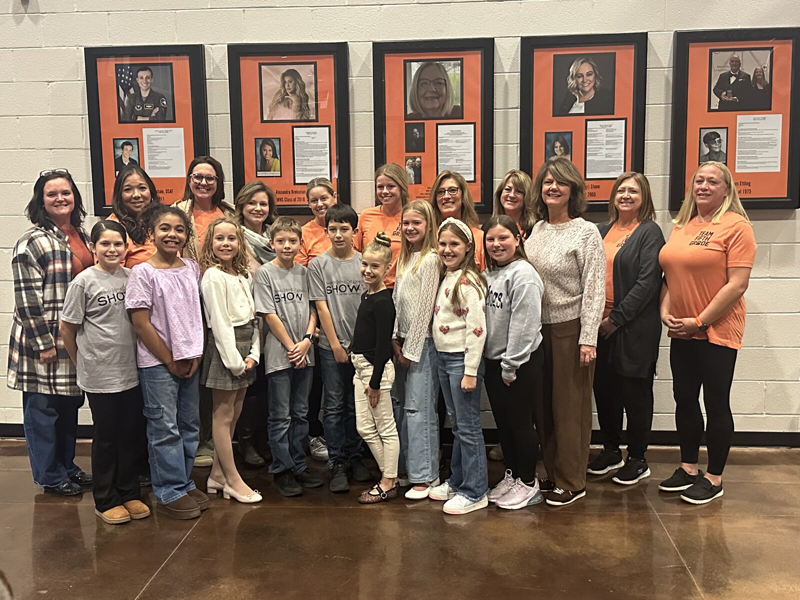 A group of students and adults pose together in front of framed portraits.