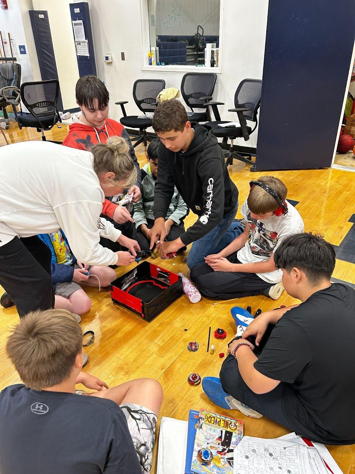 A group of children and an adult gather on a gym floor, playing with toys.