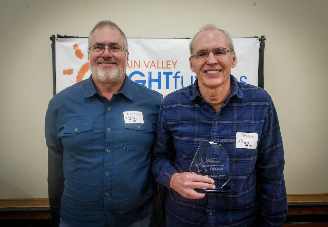 Two individuals smiling for the camera and holding an award. 