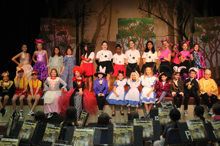 A group of children in colorful costumes pose on a stage.