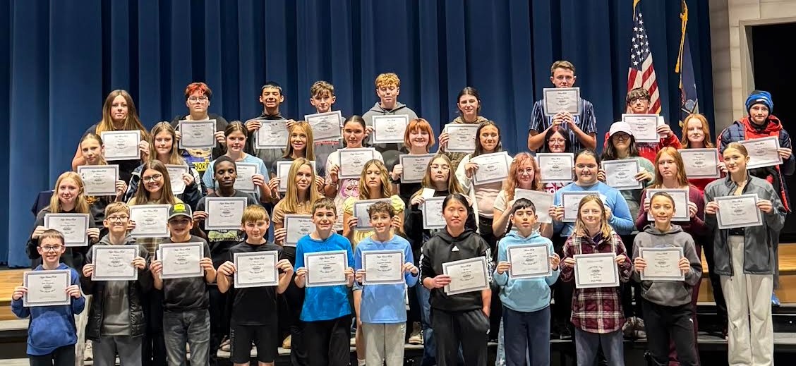 A group of students hold certificates, posing for a photo on a stage.