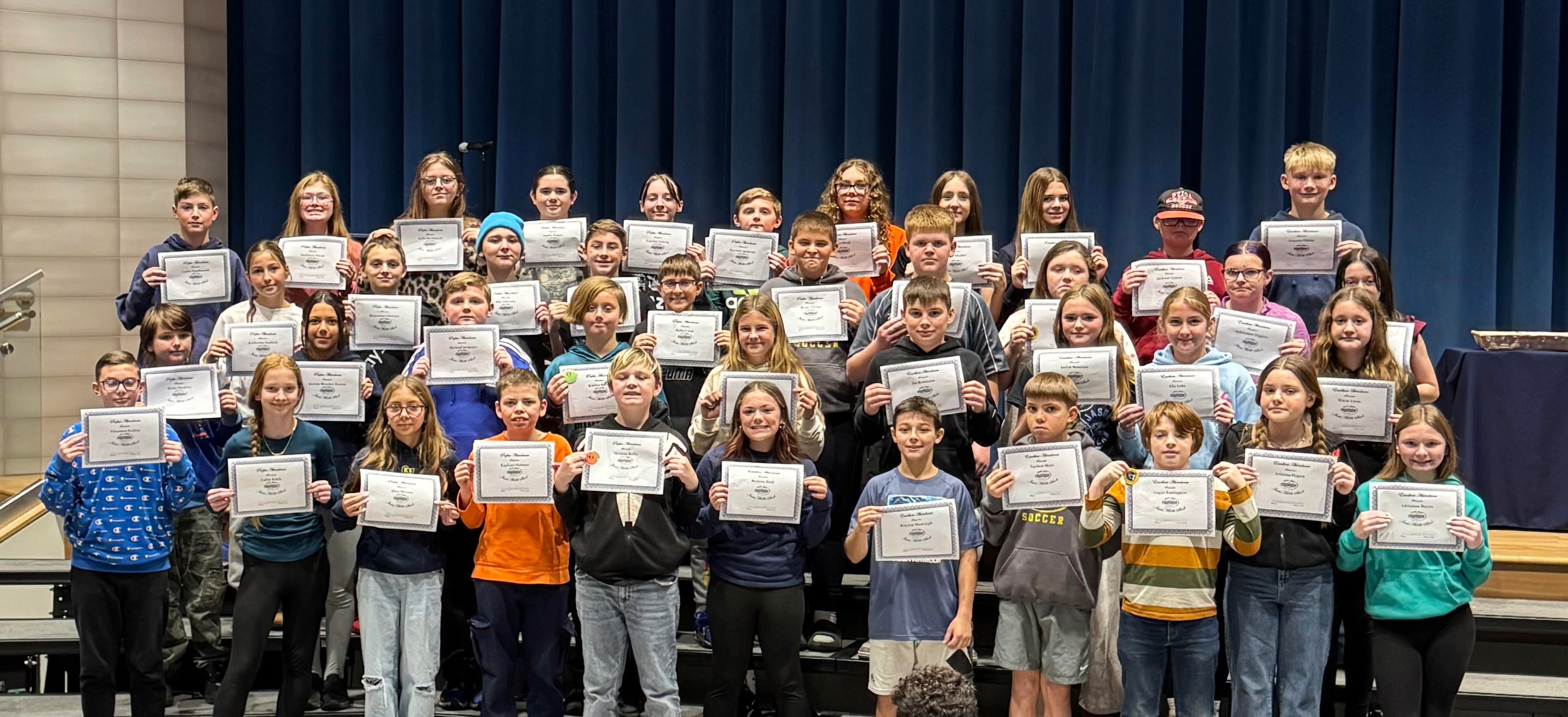 A group of students hold certificates, posing for a photo on a stage.