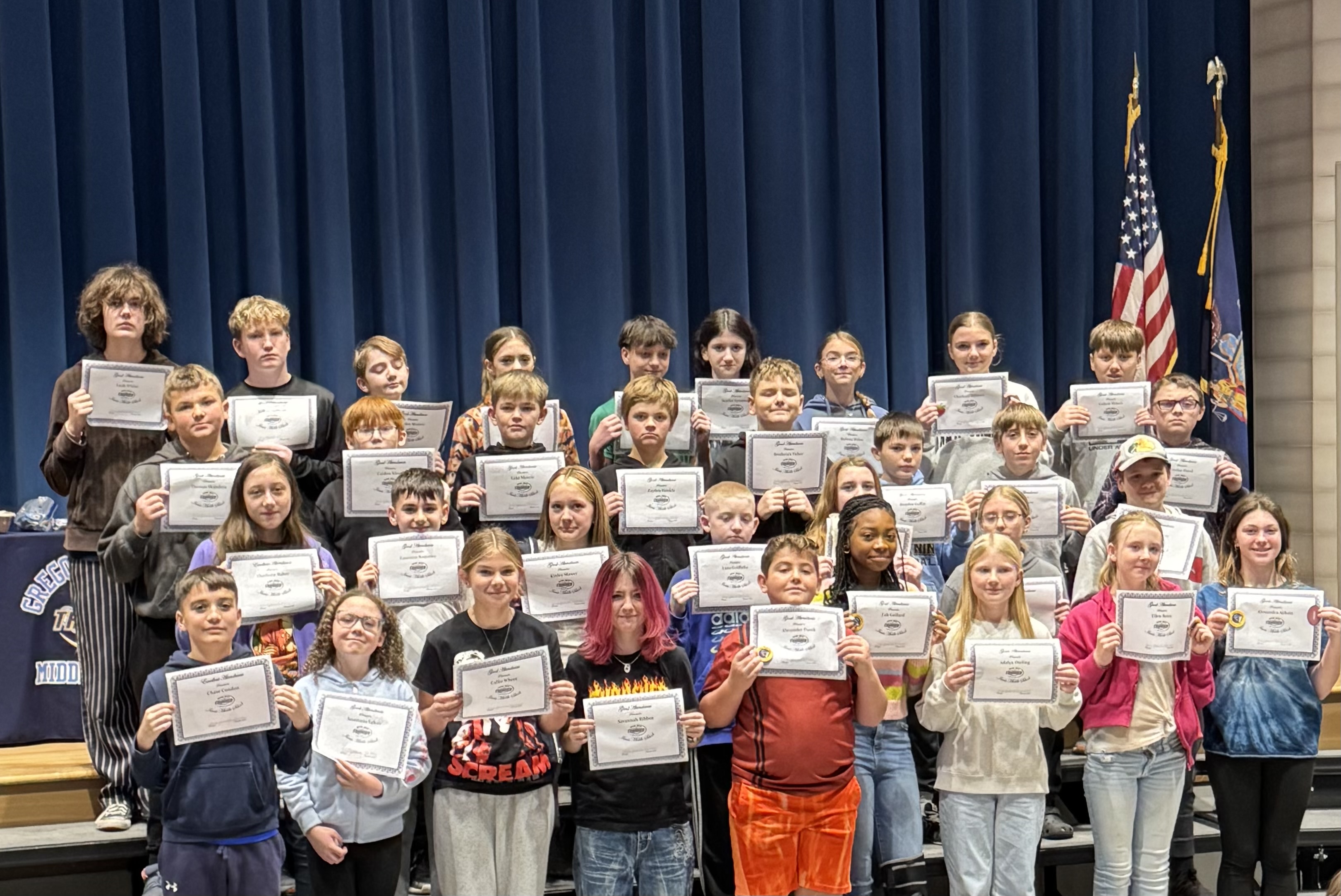 A group of students hold certificates, posing for a photo in a school setting.