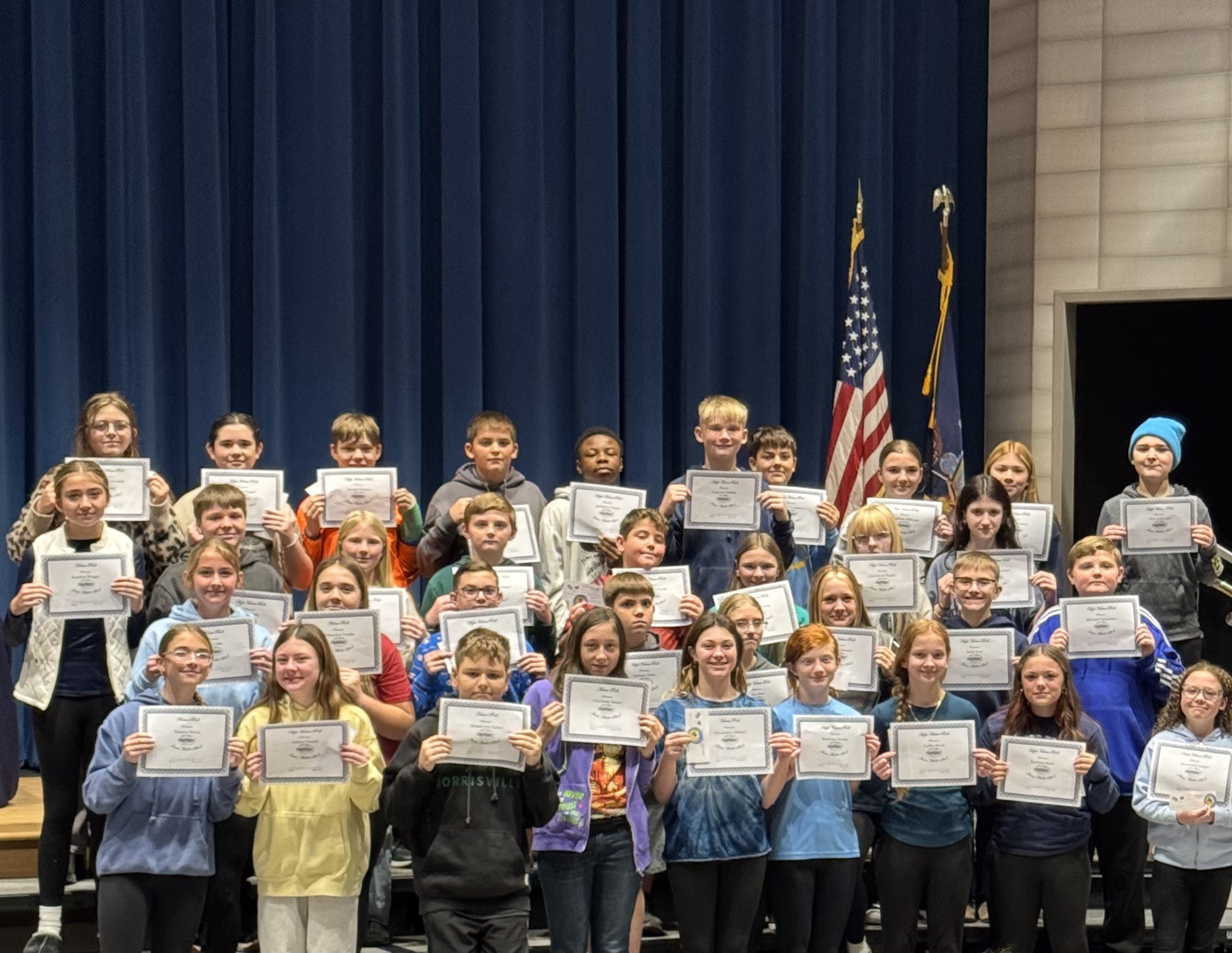 A group of students hold certificates, smiling for a photo on a stage.