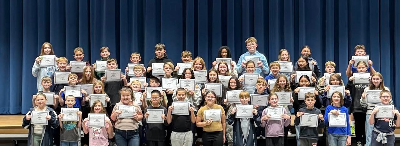 A group of students hold certificates in front of a blue curtain.