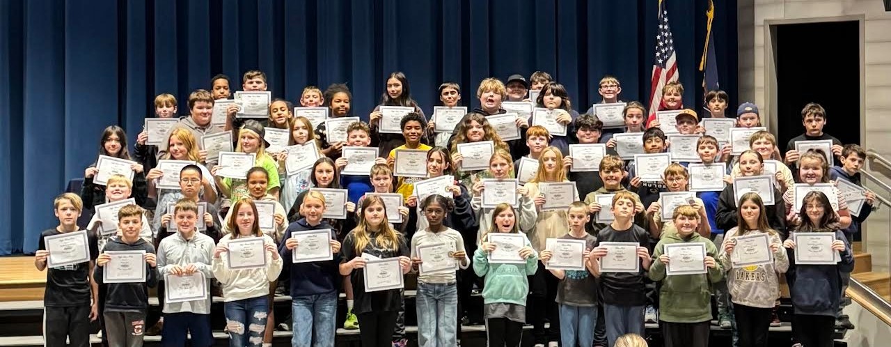 A large group of students hold certificates on a stage, smiling for the camera.