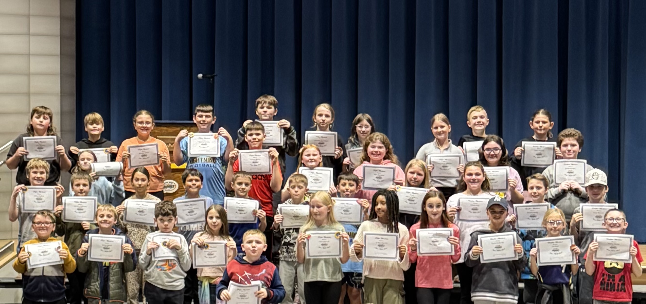 A group of students hold certificates, posing for a photo on a stage.