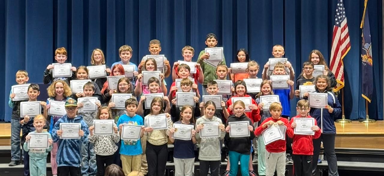 A group of students hold certificates, smiling for a photo on a stage.