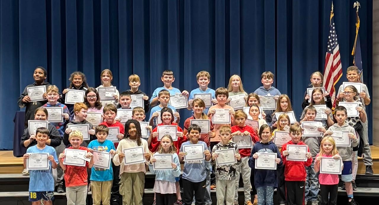 A group of students stand together, holding certificates in a school auditorium.