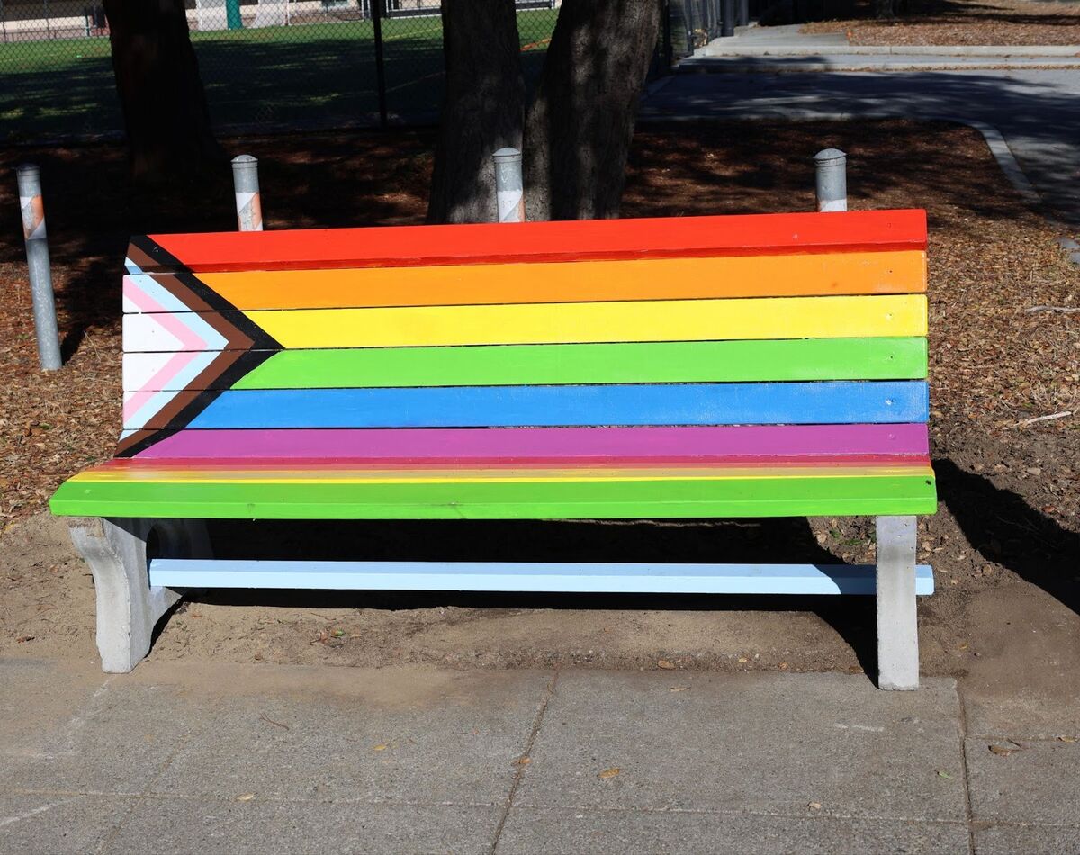 A park bench painted with the colors of the Pride flag.